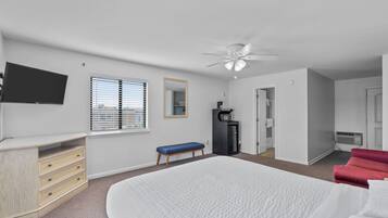 A bedroom with a bed, a desk, a chair, a television, a ceiling fan, and a window with blinds.