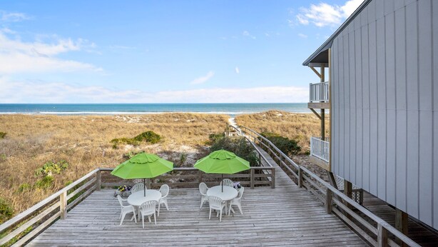 A wooden deck with white chairs and green umbrellas overlooking a beach. - The Beach House (Carolina Beach)