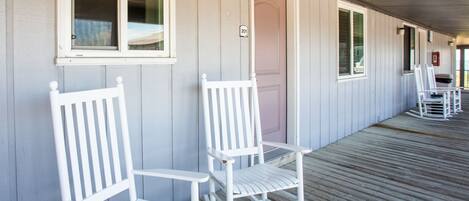 Een overdekt terras met witte houten stoelen en een deur.