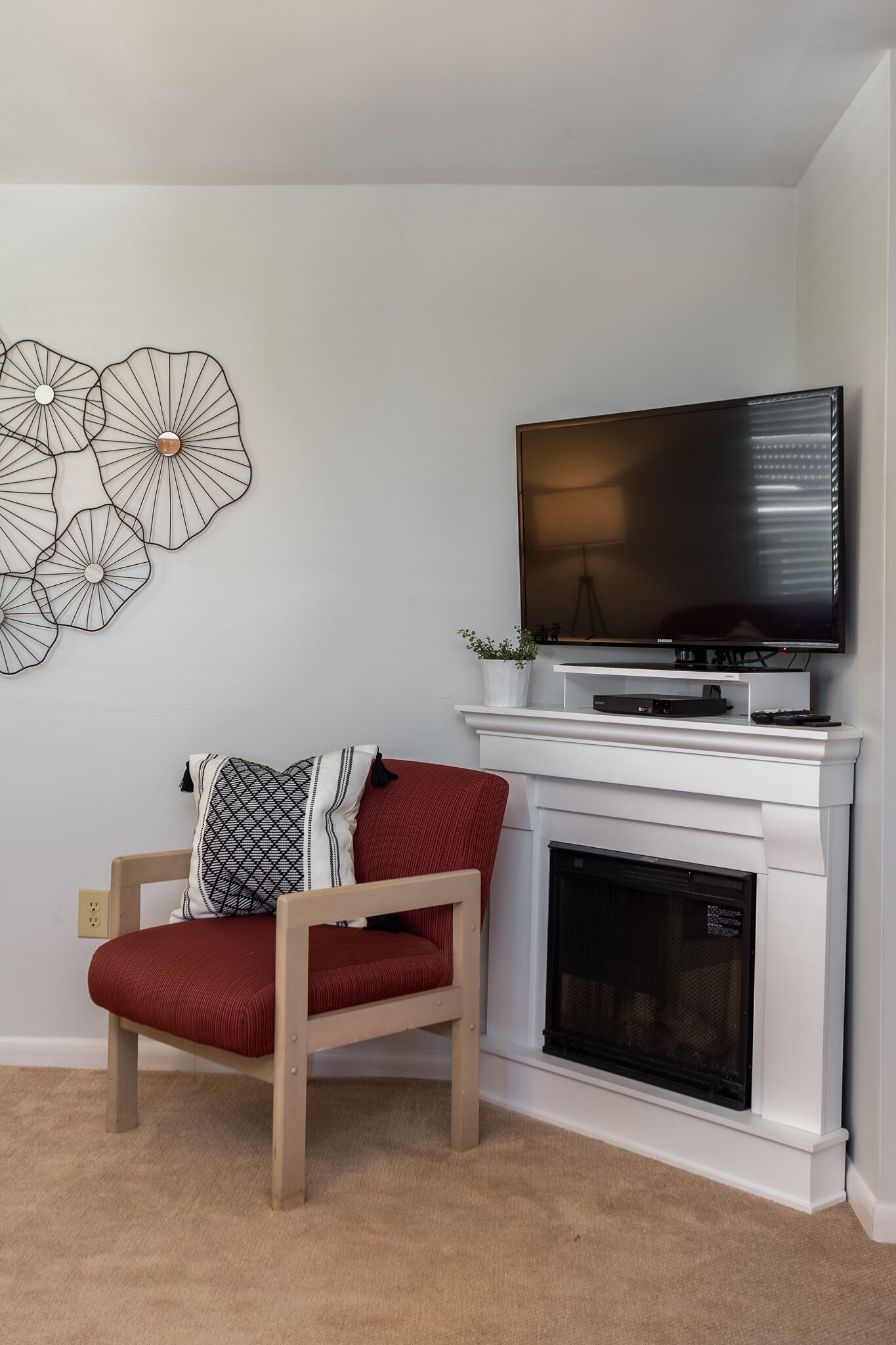 Een woonkamer met een rode fauteuil, een witte schoorsteen en een wandgemonteerde flatscreen televisie.