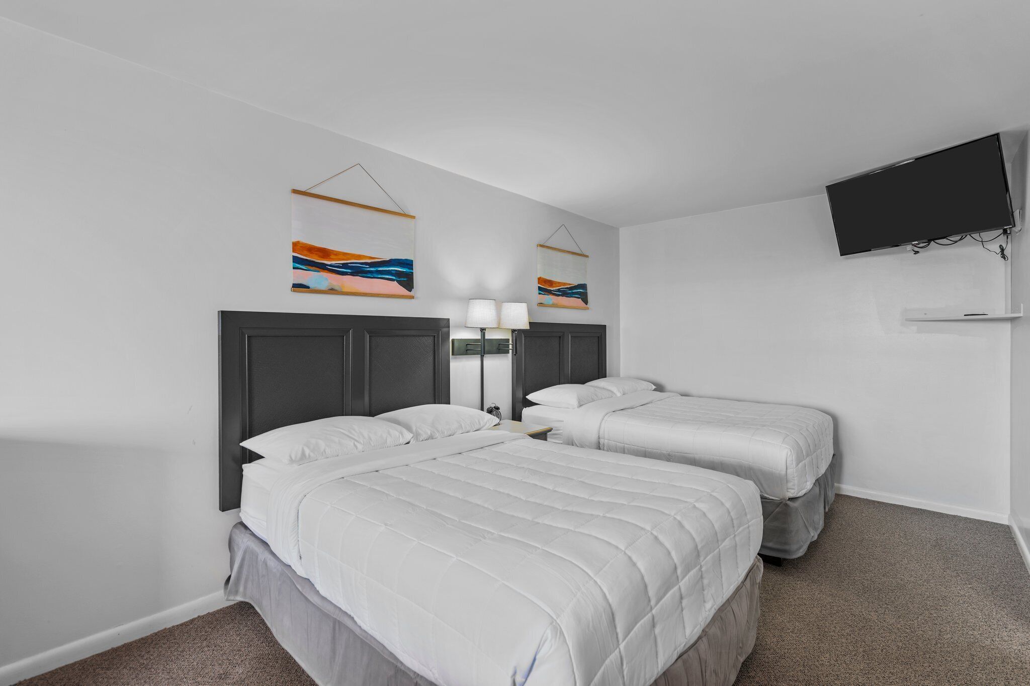 Ein Hotelzimmer mit zwei Betten, einem an der Wand montierten Fernseher und zwei abstrakten Gemälden.