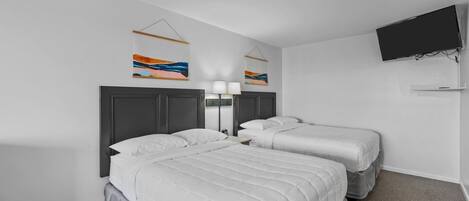Ein Hotelzimmer mit zwei Betten, einem an der Wand montierten Fernseher und zwei abstrakten Gemälden.