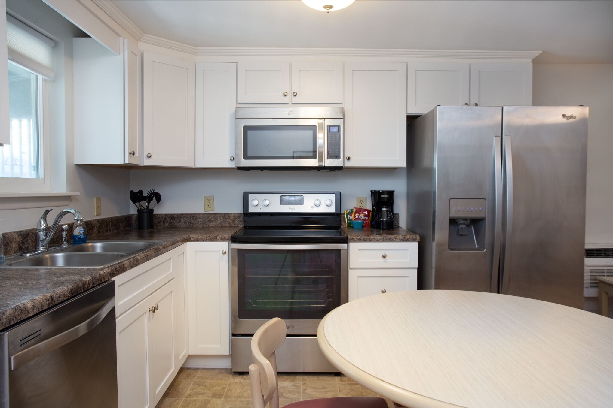A modern kitchen with white cabinets, stainless steel appliances, a granite countertop, and a dining table.