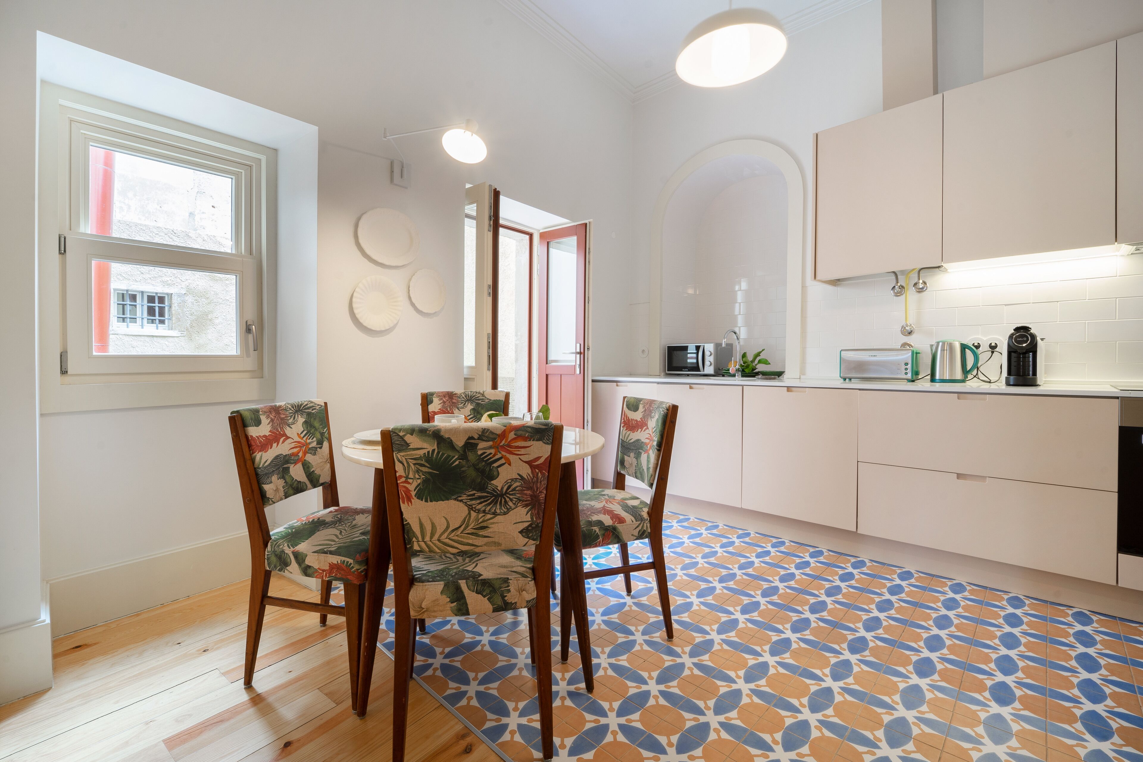 Una cocina moderna con armarios blancos, microondas, cafetera y tostadora. Hay una zona de comedor con una mesa y sillas.