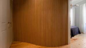 Un angle d'una habitació amb un mur de panells de fusta, un terra de fusta i un llit amb un edredó fosc al fons.