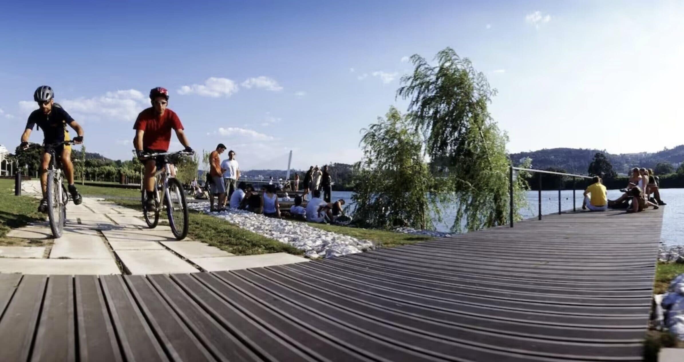 Une promenade en bois au bord d’un lac, où l’on peut voir des gens faire du vélo et s’asseoir au bord de l’eau.