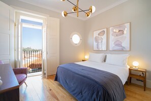 A bedroom with a bed, bedside tables, a desk, and a chair. There is a balcony with a railing and a view of the outside. - Entre Ruas Apartments (Coimbra)
