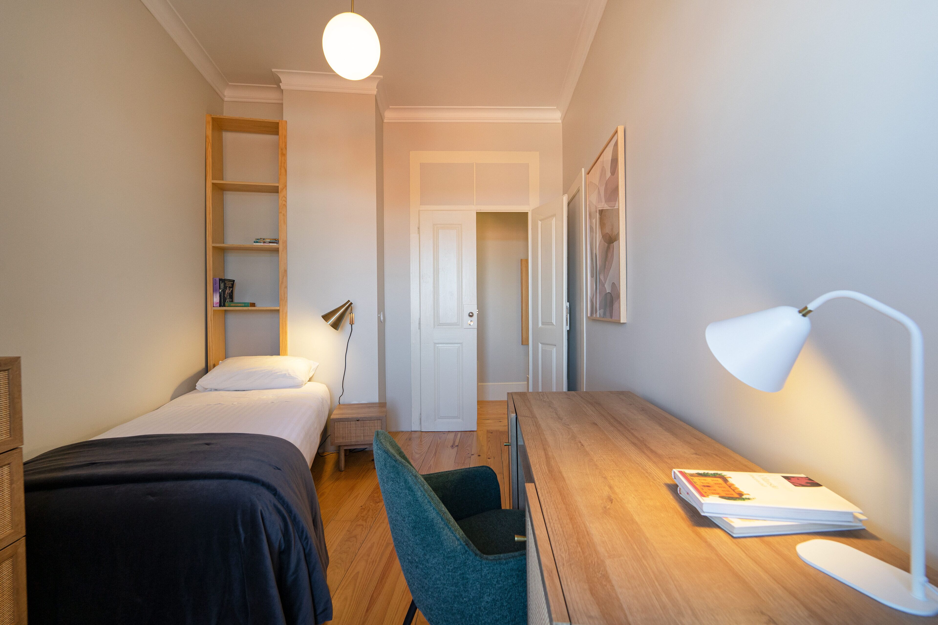 A bedroom with a bed, a desk, a chair, a lamp, and a bookshelf.