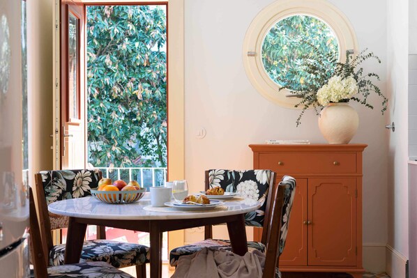 A dining area with a round table, chairs, a vase with flowers, and a cabinet. - Entre Ruas Apartments (Coimbra)