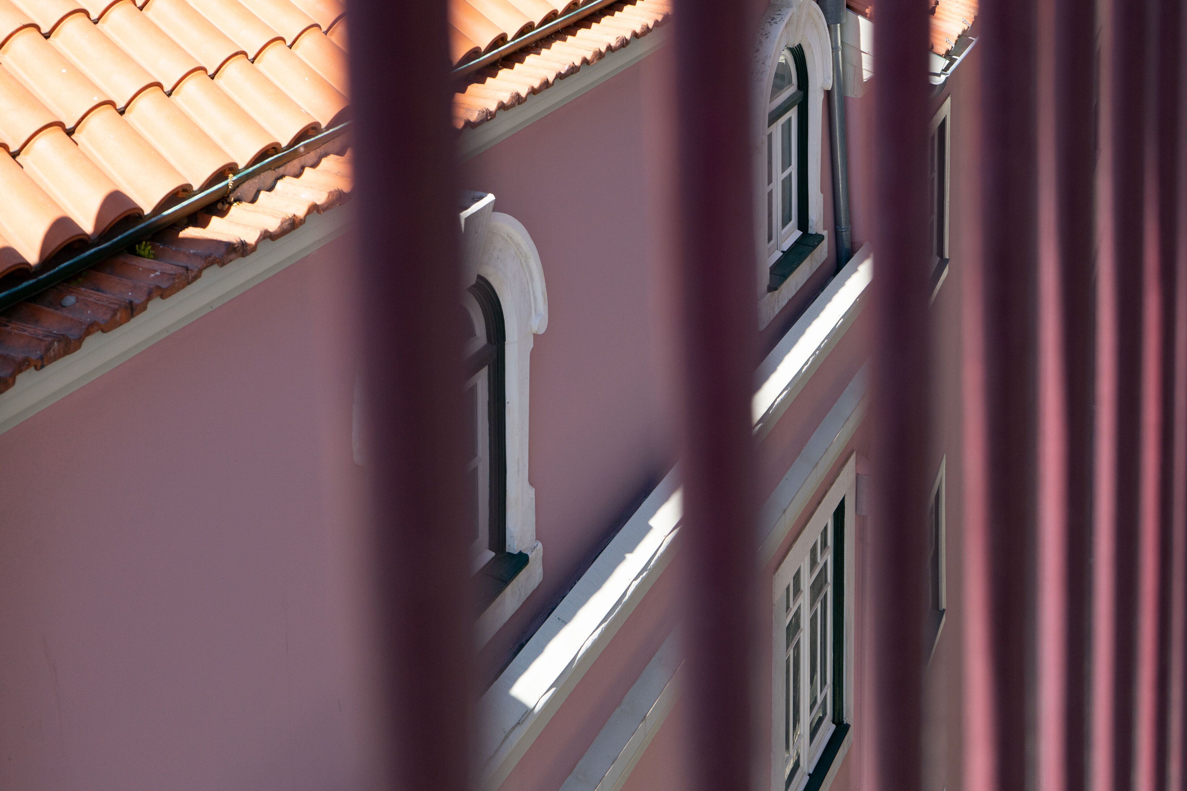 A building facade with a pinkish hue, featuring a tiled roof and arched windows.