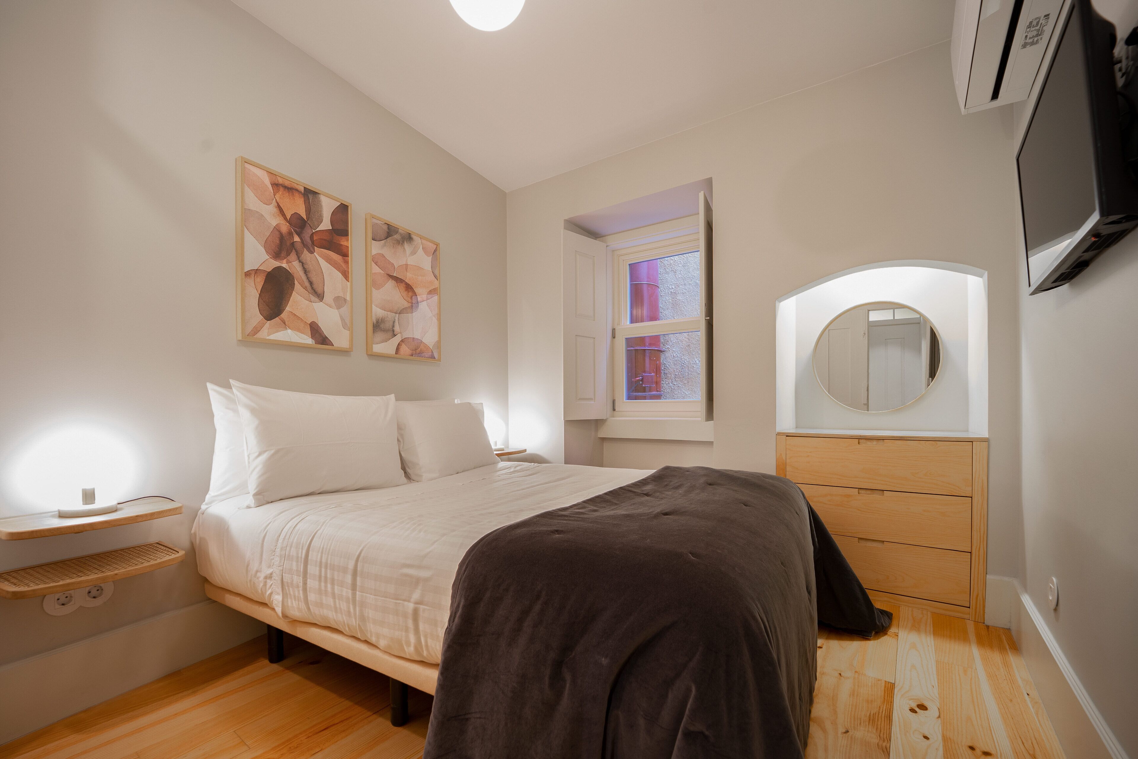 Un dormitorio con cama, mesitas de noche, cómoda, espejo y obras de arte en la pared.
