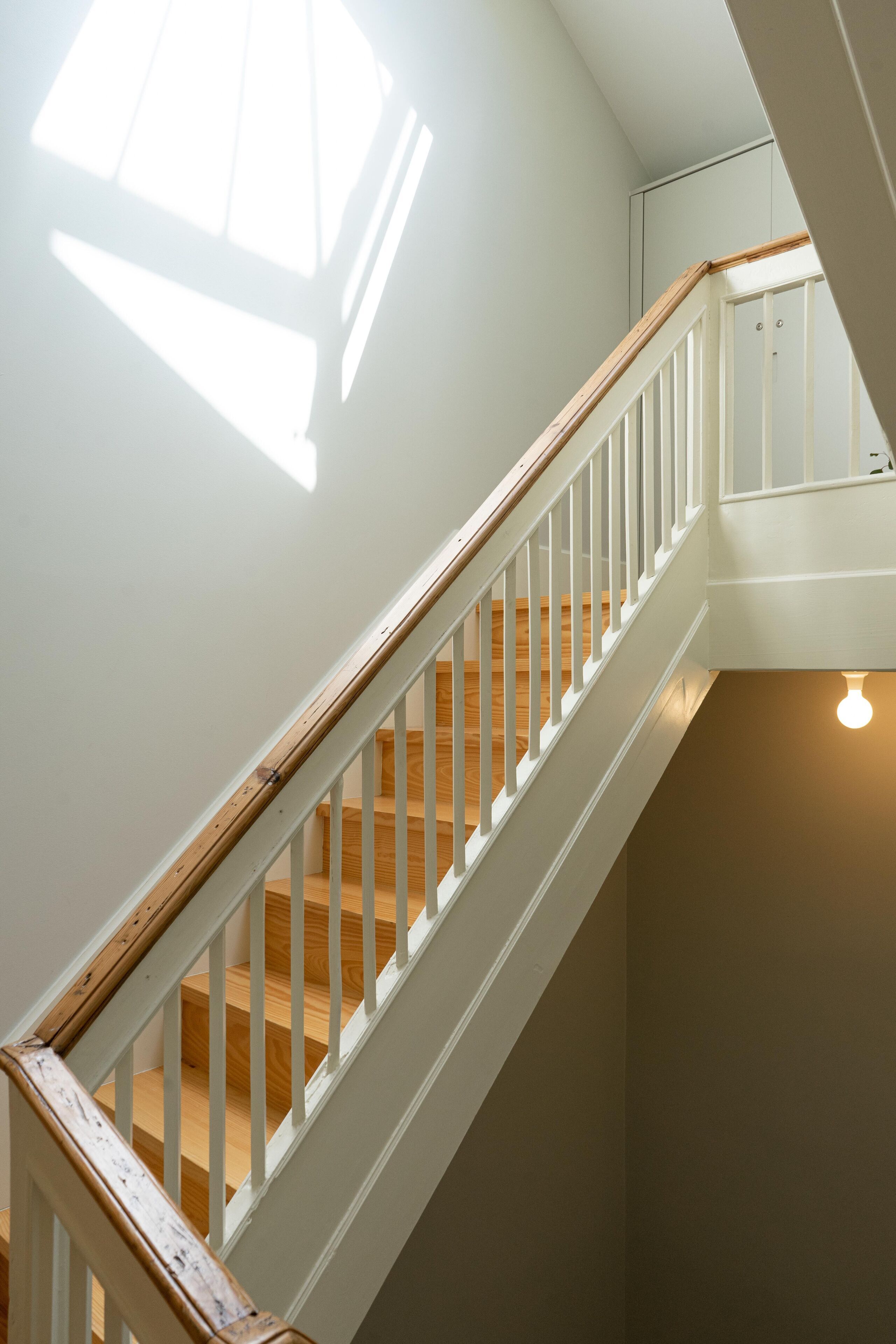 A staircase with wooden steps and white railings, leading to a landing with a light fixture.