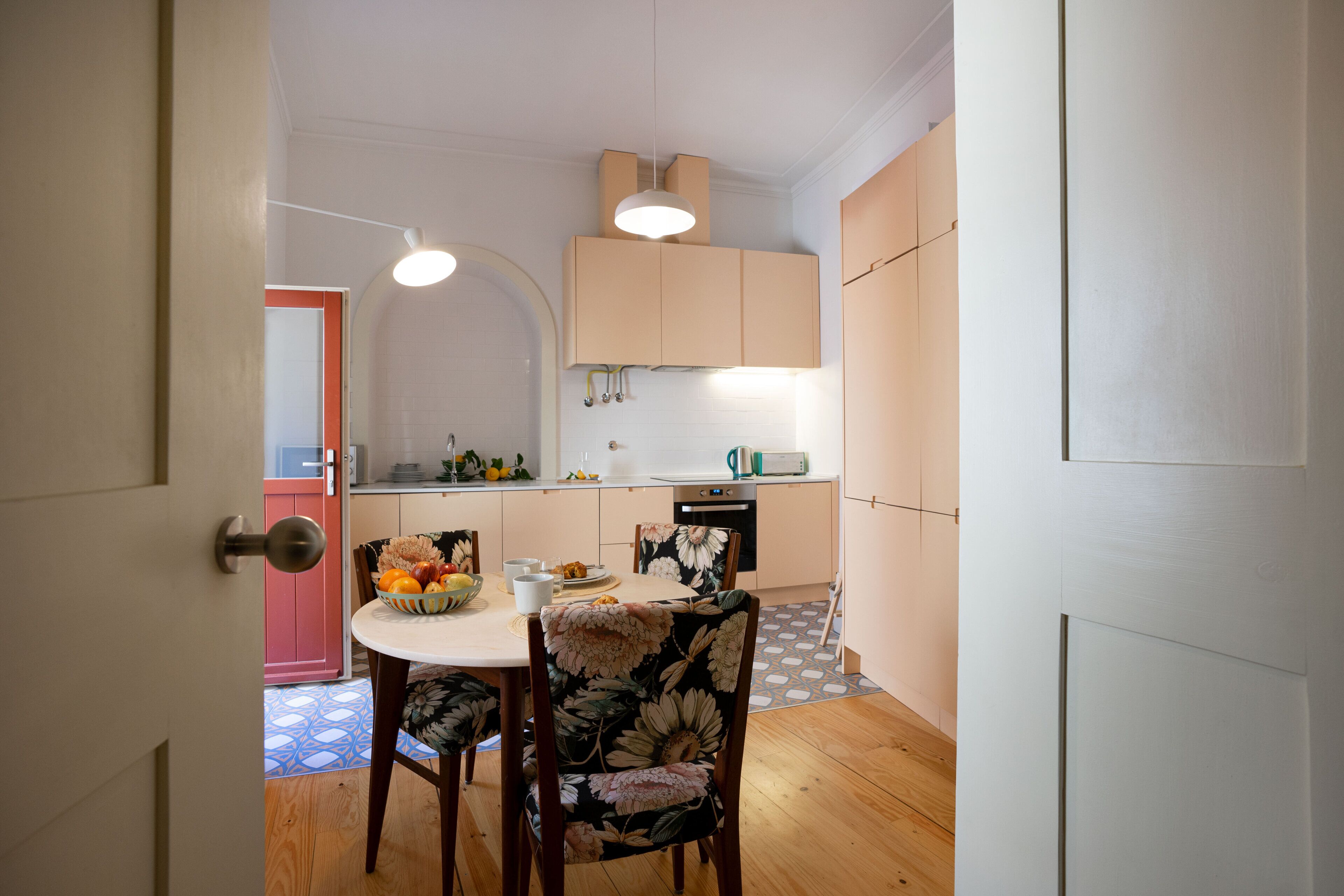 Une cuisine compacte avec un coin repas, comprenant une table blanche, des chaises à motifs floraux et un saladier à fruits.