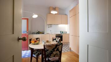 Una cocina compacta con zona de comedor, que incluye una mesa blanca, sillas con estampado floral y un frutero.