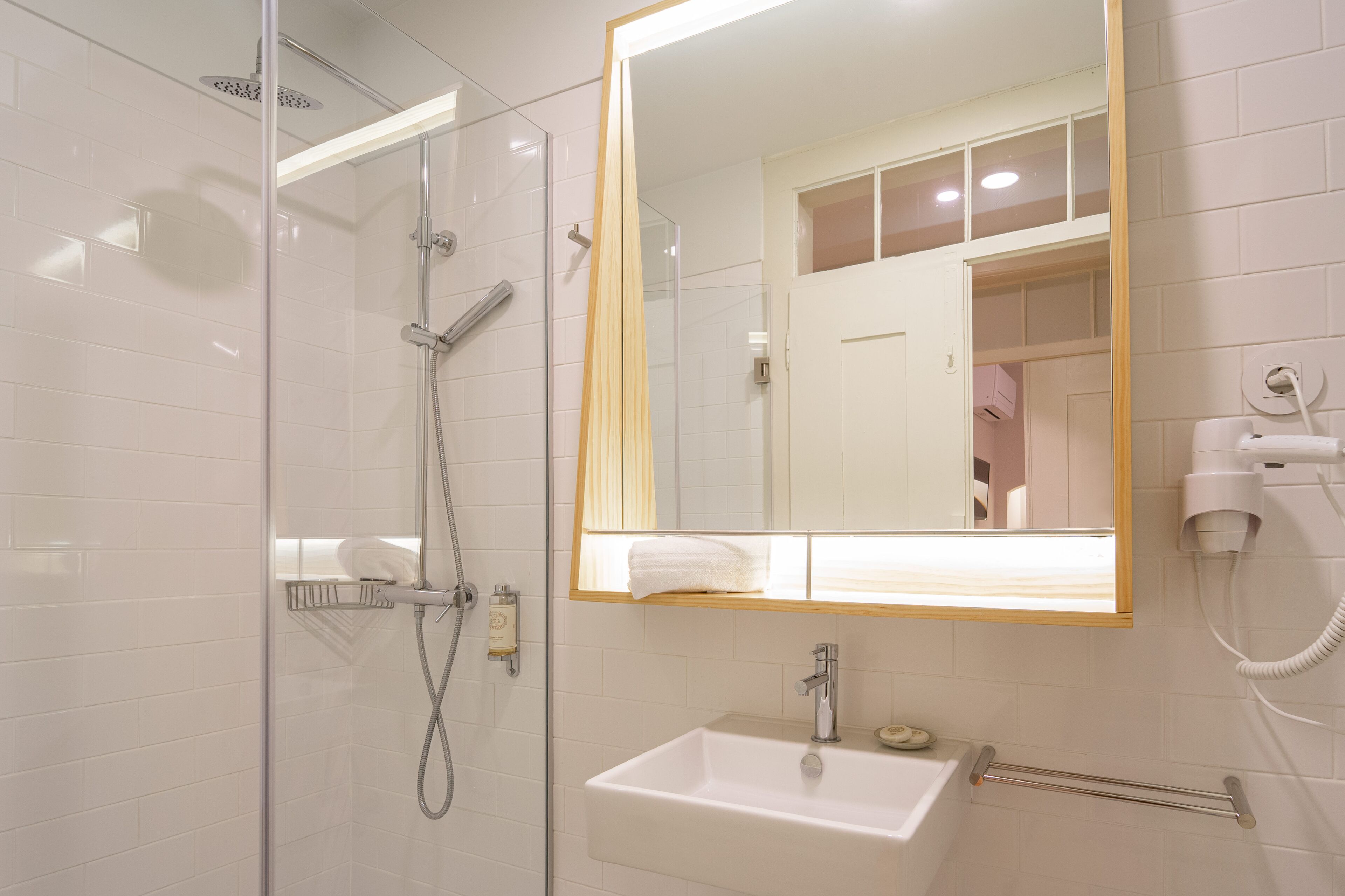 A modern bathroom with a glass-enclosed shower, a large mirror, a sink, and a hairdryer on the wall.