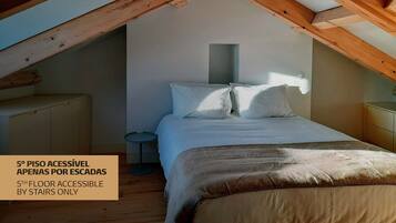 A bedroom with a sloped ceiling, a bed, a bedside table, and a small round table.