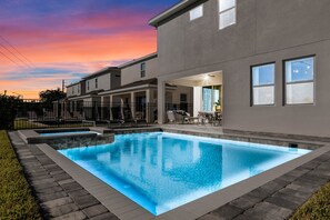 Un immeuble résidentiel moderne doté d’une piscine rectangulaire, d’un espace extérieur aménagé pour se détendre et offrant une vue sur le coucher de soleil.