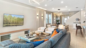Ein modernes Wohnzimmer mit einer Couch, Sesseln, einem Couchtisch und einem Fernseher.