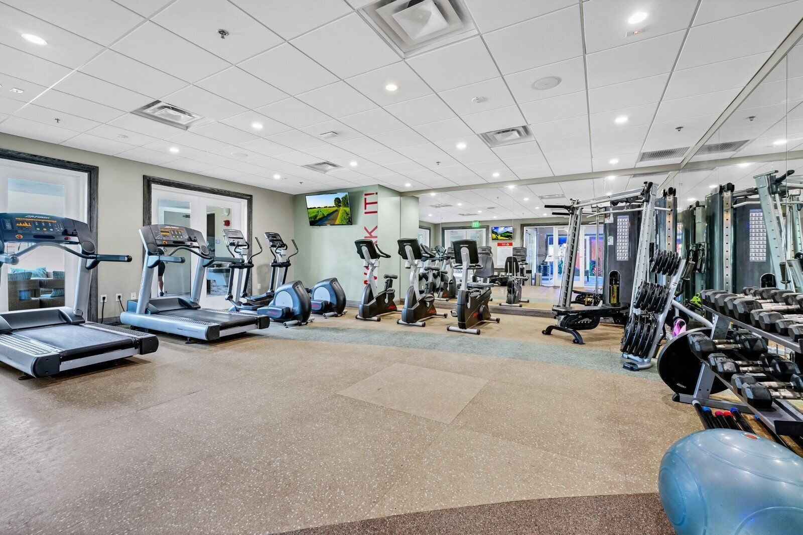Ein großzügiger Fitnessraum mit Laufbändern, Crosstrainern und Gewichten.