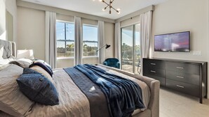 Ein modernes Schlafzimmer mit einem großen Bett, einem an der Wand montierten Fernseher und einem Balkon mit Blick.