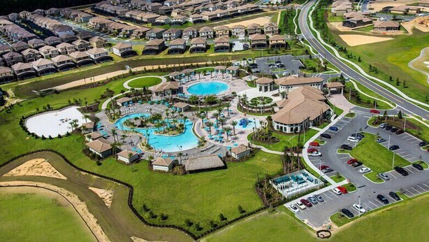 Vista aérea de una zona residencial con varias casas, un complejo grande de piscinas y un estacionamiento.