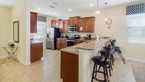 Una cocina moderna con armarios de madera, encimera de granito, electrodomésticos de acero inoxidable y una barra con taburetes.