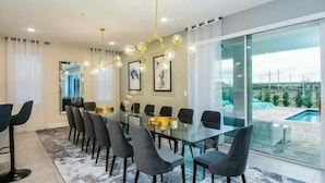 A modern dining room with a glass table, dark chairs, and a pool view.