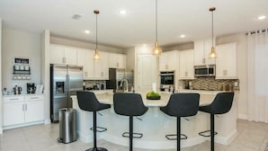 A modern kitchen with white cabinets, stainless steel appliances, and black bar stools.