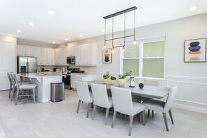 A modern kitchen with white cabinetry, a central island, and a dining area with grey chairs. - Last Minute Disney! Private Pool, Hot Tub, Game Room & Themed Bedrooms. Book Now! #65345 (Orlando)