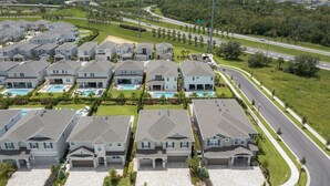 Un quartier résidentiel composé de plusieurs maisons à deux étages, d’une route sinueuse et d’un grand espace vert agrémenté d’une piscine.