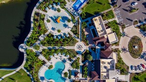 Eine Vogelperspektive zeigt ein Resort mit einem zentralen Pool, mehreren Liegebereichen und einem Parkplatz.