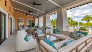 Ein überdachter Außenbereich mit Sofas und Sesseln, einem Deckenventilator und Blick auf Palmen und einen Pool.