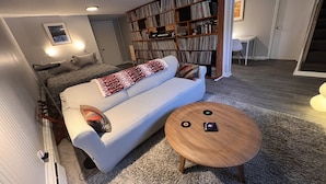 Una sala de estar con sofá, mesa de centro, estantería y cama.