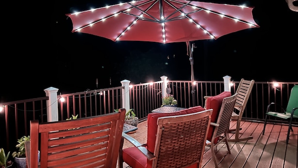 Una terraza con un paraguas rojo, sillas de madera y una mesa con plantas en macetas.
