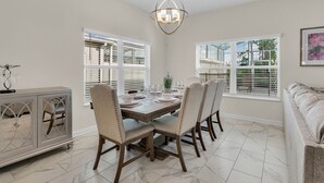 A dining area with a wooden table, four chairs, a chandelier, and large windows with blinds. - Last Minute Disney Getaway! Private Pool & Themed Bedrooms. Book Now! #65717 (Orlando)