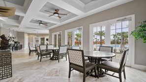 A spacious dining area with a round table and chairs, large windows with a view of palm trees, and ceiling fans.
