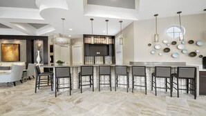 A modern kitchen with a bar area, featuring a stone backsplash, pendant lighting, and a large window.