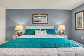 A neatly made bed with white bedding and teal accents, flanked by two bedside tables with lamps.