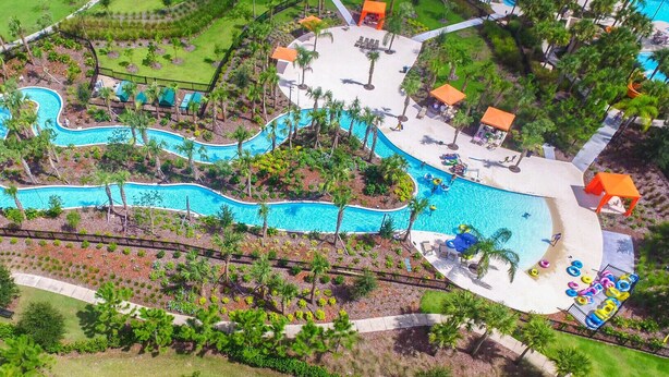 An aerial view of a resort with a winding pool, palm trees, and a sandy beach area.