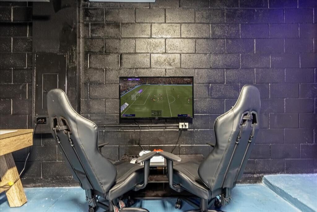 A room with two gaming chairs facing a mounted TV displaying a soccer game.