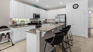 Una cocina moderna con armarios blancos, encimera de granito, refrigerador de acero inoxidable y microondas integrado.