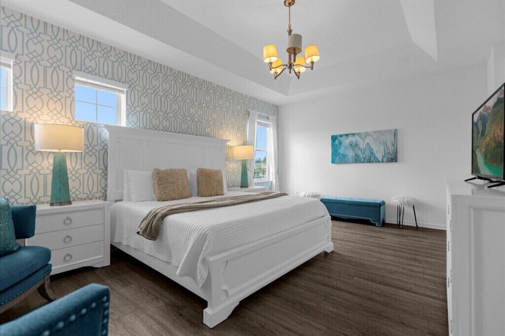 A bedroom with a large bed, two bedside tables, a chair, a bench, a TV, and a painting on the wall.