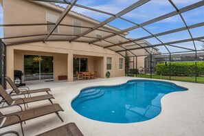 Une piscine extérieure couverte, dotée de chaises longues, d’une table de patio et d’une porte vitrée donnant sur un espace patio abrité.