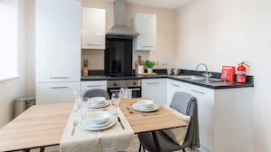 A modern kitchen with white cabinets, a black stove, and a dining table set for four. - 1 Bed Manchester Apartment with Parking - Sleeps 3 (Salford)
