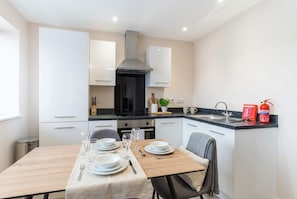 A modern kitchen with white cabinets, a black stove, and a dining table set for four.