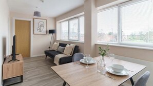 A modern living room with a sofa, a dining table set for two, and a TV on a stand. - 1 Bed Manchester Apartment with Parking - Sleeps 3 (Salford)