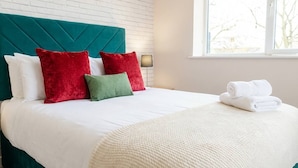 A bed with a teal headboard, white and red pillows, a green pillow, and a white blanket. - 1 Bed Manchester Apartment with Parking - Sleeps 3 (Salford)