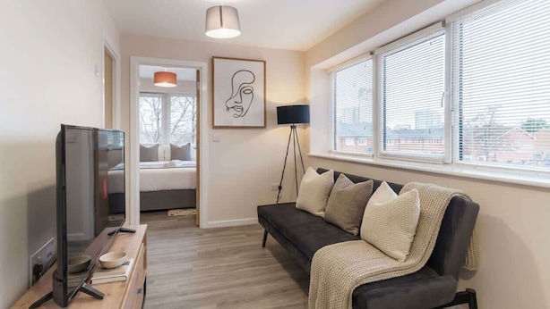 A modern living room with a sofa, a television, a lamp, and a framed artwork on the wall. - 1 Bed Manchester Apartment with Parking - Sleeps 3 (Salford)