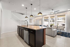 Una cocina moderna con una isla grande, armarios oscuros e iluminación colgante.