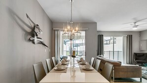 A dining area with a long table set for six, a chandelier, and a view of the outdoors through large windows. - Last Minute Disney Getaway! Private Pool & Themed Bedrooms. Book Now! #65827 (Orlando)